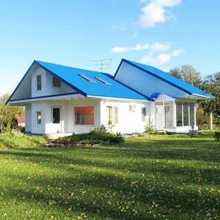 На фото: одноэтажный загородный дом белого цвета с голубой двускатной крышей, перед домом - лужайка