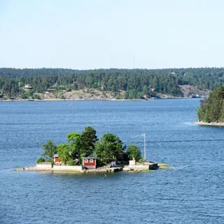 На фото: солнечный ясный день, маленький островок посреди водной глади, на острове - маленький домик и несколько деревьев, вид с борта парома