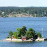 На фото: солнечный ясный день, маленький островок посреди водной глади, на острове - маленький домик и несколько деревьев, вид с борта парома
