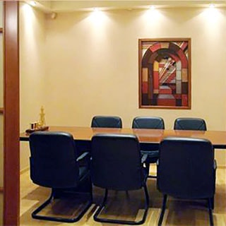 На фото: часть нежилого помещения офисного типа - переговорная комната, в комнате - большой стол для переговоров, вокруг стола - шесть офисных мягких стульев, на стене - эстамп, стены окрашены, полу - линолеум, на потолке - точечные светильники