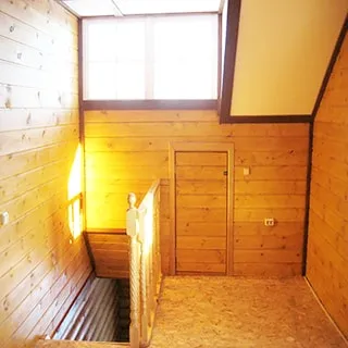 На фото: площадка на выходе лестницы в мансардный этаж, площадка огорожена резными перилами, одно высокое окно, в стене под окном дверь в кладовую, стены обшиты вагонкой