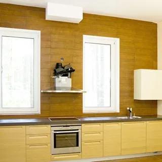 На фото: часть помещения кухни, два окна, вдоль всей стены встроенная кухонная мебель (тумбы-столы) с общей столешницей, в середине - электрическая варочная поверхность, над ней - вытяжка, под ней - духовой шкаф, правее - металлическая мойка со смесителем, окна - стеклопакеты, полы и стена - плитка, потолок - окрашен в белый цвет