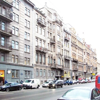 На фото: фасад пятиэтажного кирпичного многоквартирного жилого дома, фасад оштукатурен, эркеры, балконы, перед домом - проезжая часть, тротуар, припаркованные и движущиеся автомобили