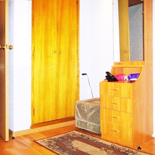 На фото: часть помещения прихожей, встроенный шкаф для одежды, пуф, небольшой комод со шкафчиком в полный рост с зеркальной дверцей, стены оклеены обоями, на полу - коврик