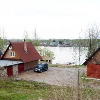 На фото: вид на комплекс с тыльной стороны, на переднем плане - баня с пристроенным гаражом, справа - жилой деревянный одноэтажный дом, между ними - отсыпанная площадка для стоянки автомобилей, на заднем плане - берег реки и река