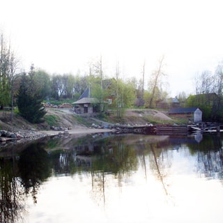 На фото: вид на комплекс с воды, берег с коротким крутым уклоном, каменисто-песчаный, на высокой его части - беседка, на берегу у кромки воды - деревянный эллинг, устроен пирс