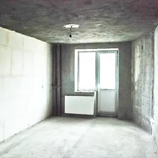На фото: часть помещения комнаты, одно окно с балконной дверью, стеклопакет, под окном - батарея центрального отопления, стены, потолок и пол выровнены и подготовлены под чистовую отделку
