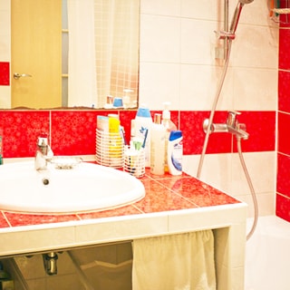 На фото: часть помещения ванной комнаты, керамическая раковина со смесителем вмонтирована в столешницу, облицованную плиткой, над ней - зеркало, справа ванная со смесителем для ванной, стены облицованы керамической плиткой