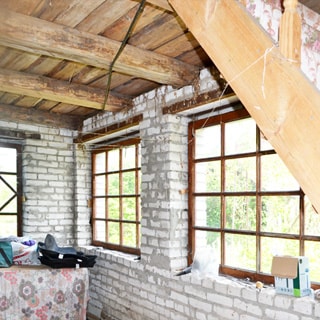 На фото: часть внутреннего помещения дома, без внутренней отделки, межэтажное перекрыте - доски по деревянным балкам, в окнах одинарные верандные рамы, на переднем плане справа - деревянная лестница на верхний этаж
