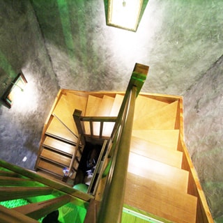 На фото: вид на лестницу и лестничный пролет с высоты площадки второго уровня, три пролета по 5-6 ступенек по периметру лестничного пролета, перила и ступеньки деревянные, на стенах пролета - светильники