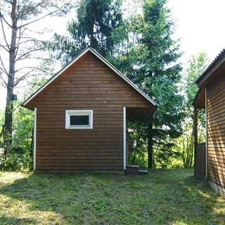 На фото: придомовая территория участка, справа - стена дома, прямо - деревянная баня с крыльцом, участок покрыт травой, за баней - деревья