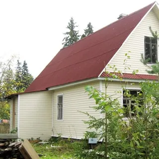 На фото: жилой одноэтажный дом, двускатная крыша, фасад облицован сайдингом, входной тамбур, перед домом газон, деревья