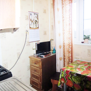 На фото: кухня, окно со стеклопакетом, плита - газовая, у окна тумба с телевизором, обеденный стол, табурет, стены оклеены обоями