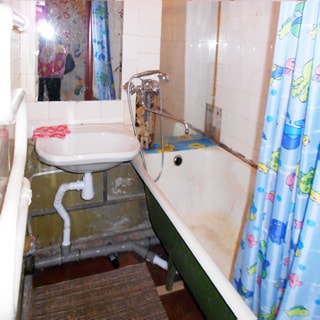 На фото: часть помещения ванной комнаты, прямо у стены - керамическая раковина, над раковиной - зеркало, слева на стене - полотенцесушитель, справа - ванная, смеситель общий для ванны и раковины, стены облицованы керамической плиткой