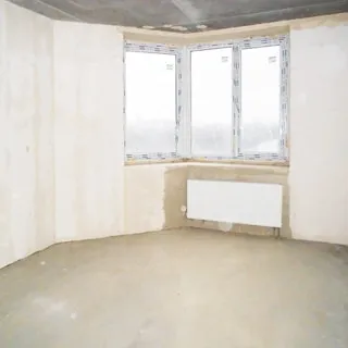 На фото: помещение жилой комнаты под чистовую отделку, одно трехстворчатое угловое окно, установлен стеклопакет, под окном - батарея центрального отопления, стены оштукатурены, полы - цементно-песчаная стяжка