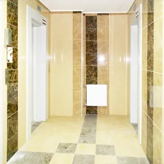 На фото: помещение лифтового холла, четыре лифта, стены и полы отделаны керамической плиткой, прямо у стены - батарея центрального отопления