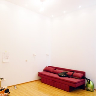На фото: часть помещения, полы - ламинат, стены и потолок окрашены в белый цвет, на потолке - точечные светильники, в углу - мягкий диван-кровать, справа от него на полу - пылесос