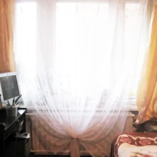 На фото: часть помещения жилой комнаты, большое трехстворчатое окно, под окном - батарея центрального отопления, слева от окна - компьютерный столик, на столе - монитеор компьютера, справа от окна у стены - диван-кровать
