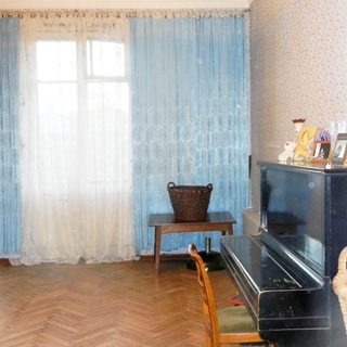 На фото: часть помещения жилой комнаты, одно окно, справа у окна - журнальный столик, справа у стены - пианино со стулом, стены оклеены обоями, пол - паркет