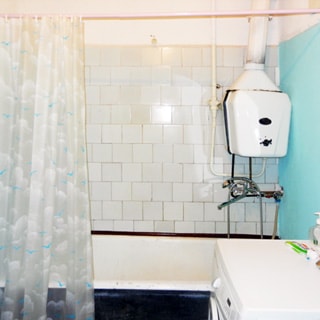 На фото: часть помещения ванной комнаты, впереди у стены - ванная со смесителем и газовой колонкой, справа у стены - стиральная машина, стена у ванной облицована керамической плиткой, стена справа - окрашена