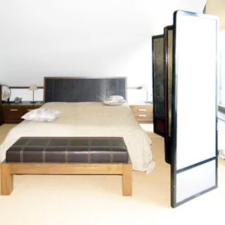 На фото: часть жилого помещения - спальни в мансардном этаже, посреди помещения - двуспальная кровать, слева у стены - тумбы и шкафы для одежды, справа - окно, между окном и кроватью - ширма
