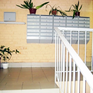 На фото: часть помещения парадной со стороны входа, лестница с металлическими перилами с деревянной накладкой, полы и ступени облицованы керамической плиткой, стены - окрашенный кирпич, прямо на стене - блок почтовых ящиков