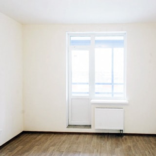 На фото: часть помещения комнаты, окно с балконной дверью, под окном - радиатор батареи центрального отопления, белые стены и потолок, полы - ламинат, комната пустая, без мебели