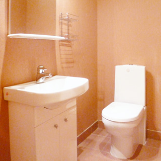 На фото: помещение туалета, прямо у стены - унитаз - компакт, слева у стены на тумбе - керамическая раковина со смесителем, над раковиной - зеркало с полкой, пол облицован керамической плиткой