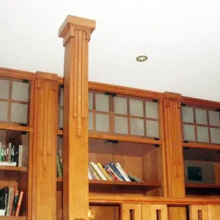 На фото: часть помещения жилой комнаты, прямо у стены от края до края - книжные шкафы, перед шкафом - деревянная колонна до потолка, на потолке - точечные светильники