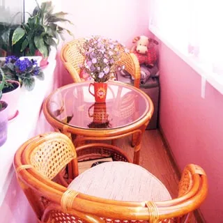 На фото: часть помещения застекленной лоджии, два плетеных деревянных кресла и круглый журнальный столик со стеклянной столешницей, комнатные растения - на подоконнике
