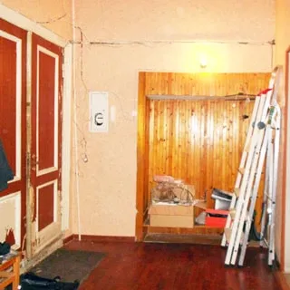На фото: помещение прихожей, слева - входная двустворчатая деревянная дверь, справа от двери в ящике в стене - электросчетчик, справа от него - место для верхней одежды, правее у стены - лестницы-стремянки, полы - ламинат