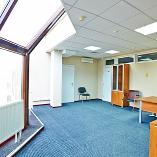 На фото: часть помещения офиса, слева большое панорамное окно от пола до потолка, полы - ковролин, потолки - подвесные с вмонтированными блоками ламп дневного освещения, на стене - кондиционер, две двери в соседние помещения, офисный шкаф, стулья, столы