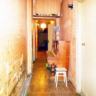 На фото: вытянутое в длину помещение коридора, слева - стена с обшарпаными обоями, справа двери в соседние помещения, слева от первой на стене - электросчетчик, справа у стены - пианино, под потолком - антресоль, закрытая шторкой, полы - паркет
