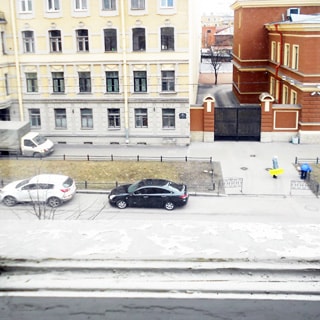На фото: вид из окна на улицу, проезжая часть с припаркованными автомобилями, вершина дерева, огороженный газон и тротуар у дома напротив