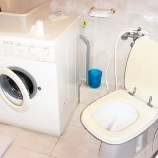 На фото: часть помещения санузла, подключенная стиральная машина с боковой загрузкой, унитаз - компакт с гигиеническим душем, полы и стены облицованы керамической плиткой