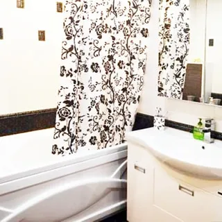 На фото: часть помещения ванной комнаты, прямо у стены в углу - ванная, спрва от нее - керамическая раковина на тумбе белого цвета с дверцами, над раковиной - шкафчик с зеркальными дверцами, стены облицованы керамической плиткой