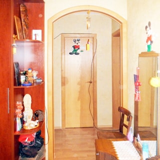 На фото: часть помещения коридора и прихожей, слева у стены - одежный шкаф, с боковыми открытыми полками, справа у стены - комод с зеркалом, слева от комода - стул, в центре впереди и справа деревянные двери в другие помещения