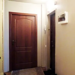 На фото: часть помещения прихожей, дверь в комнату, справа от нее - входная дверь в квартиру, слева от входной двери на стене - трубка домофона, справа от двери на стене - ящик с электрооборудованием, на полу - ковер