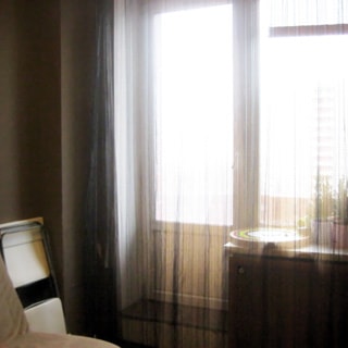 На фото: часть помещения жилой комнаты, одно с балконной дверью, слева от окна - складной стул у стены, мягкий диван или кресло