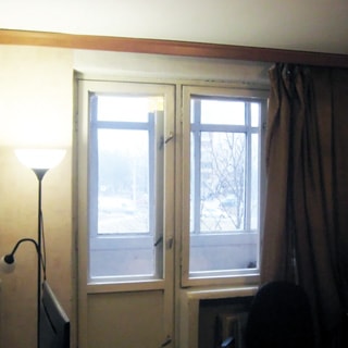 На фото: часть помещения жилой комнаты, одно с балконной дверью, за окном - застекленная лоджия, под окном - радиатор центрального отопления, слева от окна - торшер