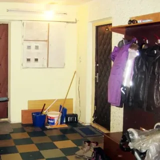 На фото: часть помещения лестничной площадки перед входом в квартиру, справа от двери - вешалка для верхней одежды с тумбой для обуви, слева от двери - закрытый щиток с электросчетчиками, полы - линолеум