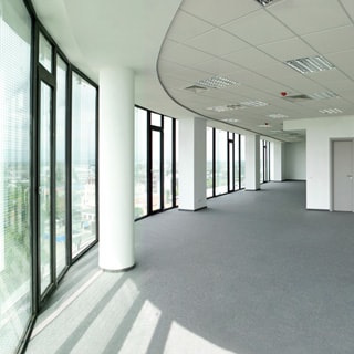 На фото: светлый просторный холл офисного помещения, слева сполшное остекление от пола до потолка, потолки навесные с встроенными светильниками, полы - ковролин серого цвета