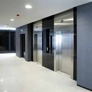 На фото: лифтовый холл, два лифта, выход на пожарную лестницу, на потолке - датчик пожарной сигнализации, встроенные светильники