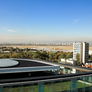 На фото: вид с высоты здания бизнес-центра на городские кварталы и аэропорт, городские постройки, сооружения и площадки аэродрома, самолеты на стоянках