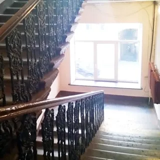 На фото: часть лестничного пролета, широкая просторная, чистая и светлая лестница, трехстворчатое окно, деревянные перила на литых узорных стойках, справа у окна - радиатор центрального отопления