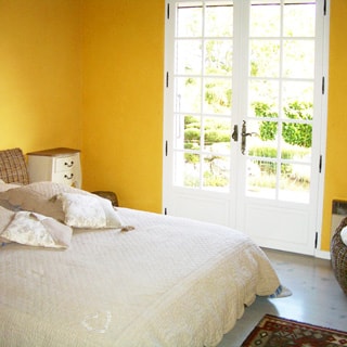 На фото: часть помещения спальни, двуспальная кровать, прикроватная тумбочка, верендная дверь с выходом в сад