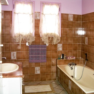 На фото: часть помещения ванной с двумя окнами, слева умывальник, справа - ванная со смесителем, полы и стены - плитка