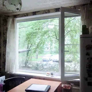 На фото: часть помещения кухни, открытое большое трехстворчатое окно во двор, слева от окна - газовая плита, у окна - стол со стулом, справа от окна - холодильник, под окном - радиатор центрального отопления, на потолке - люстра