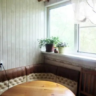 На фото: часть помещения кухни, окно с высоким подоконником, у окна - мягкий уголок и обеденный стол, стены облицованы плиткой