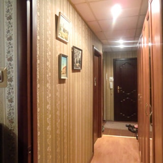 На фото: часть помещения прихожей и коридора, стены оклеены обоями, металлическая входная дверь, полы в коридоре - ламинат, в прихожей - плитка, на потолке - точечные светильники